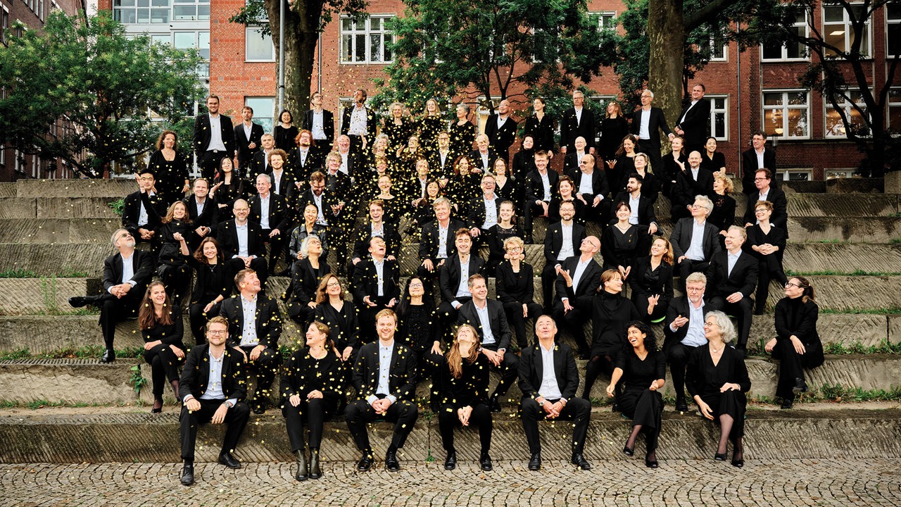 Das Orchester der Bremer Philharmoniker auf einer Treppe mit goldenem Konfettiregen.