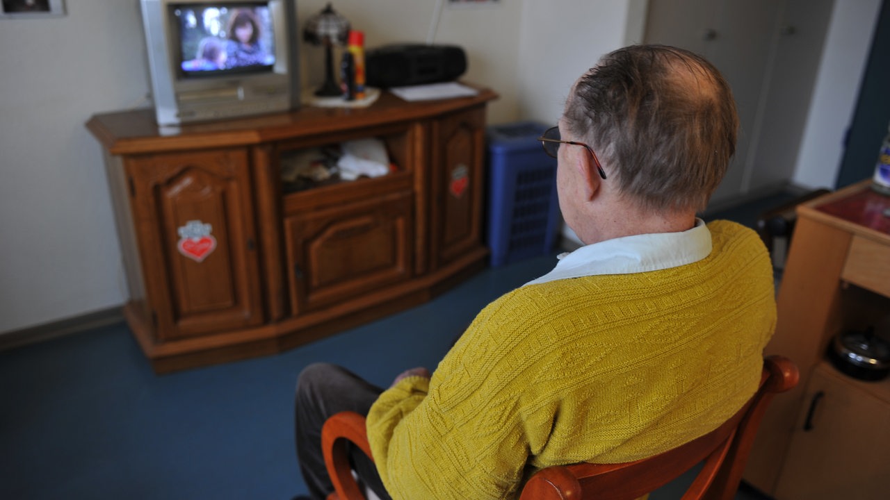 Eine älterer Mann sitzt vor einem Fernseher.