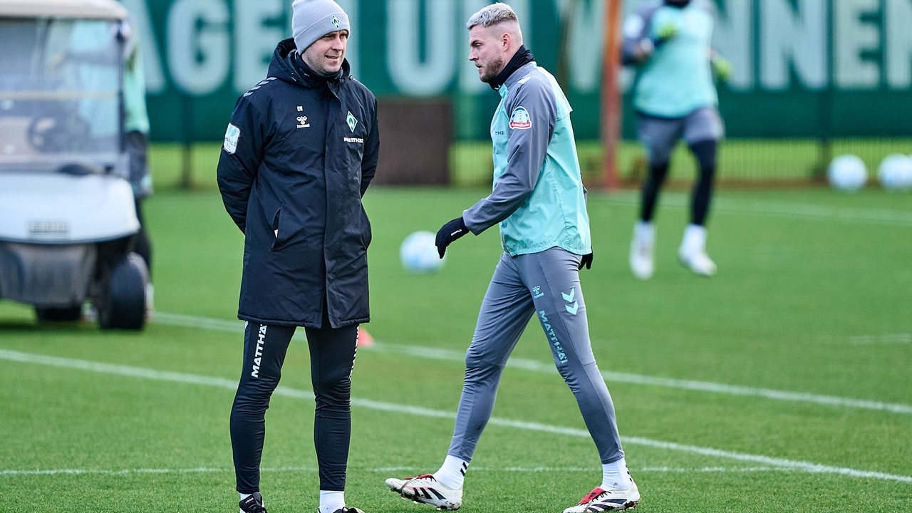 Werder-Trainer Ole Werner schmunzelt am Rande des Trainings, als Marvin Ducksch vorbeigeht.