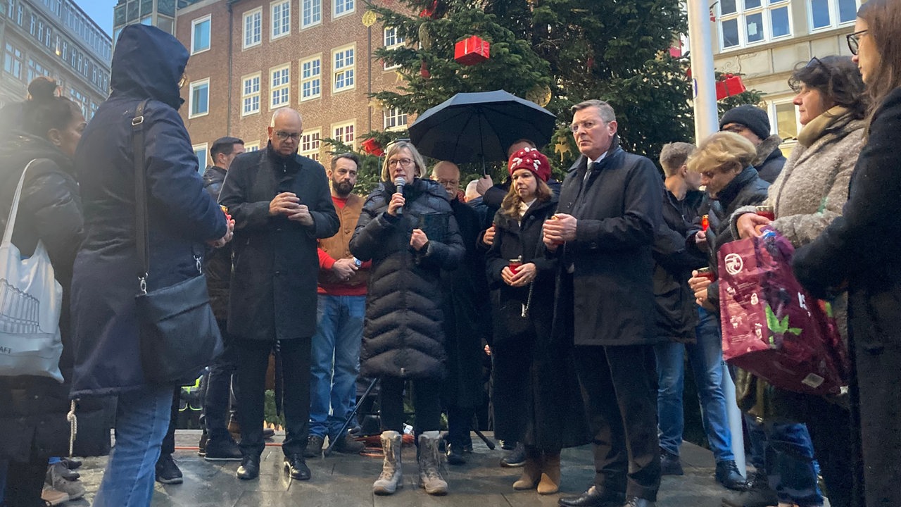 Auf dem Bremer Weihnachtsmarkt gedenken Menschen vor dem Weihanchtsbaum.