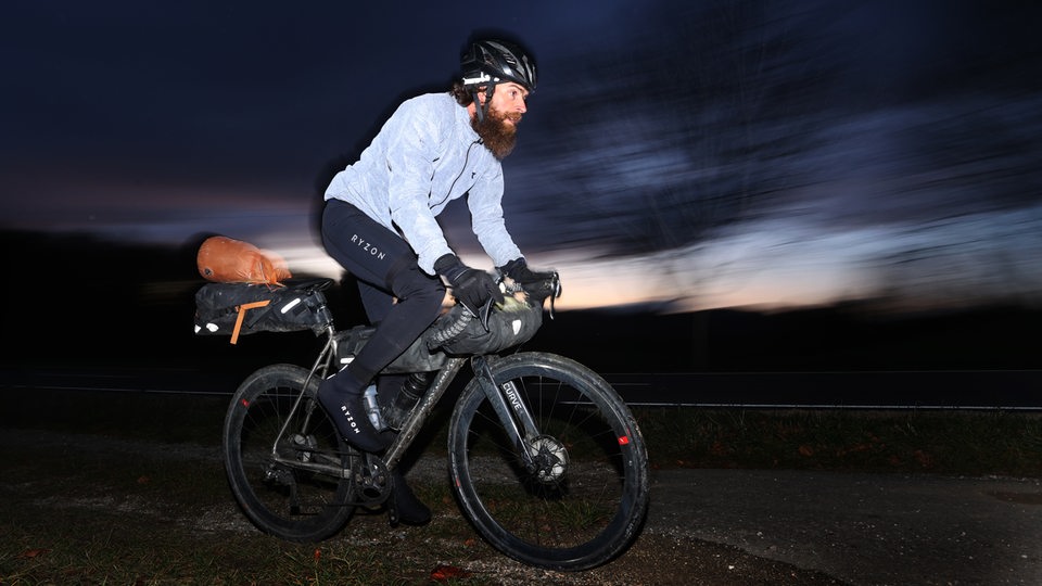 Extrem-Sportler Jonas Deichmann fährt nach seiner Grenzüberfahrt aus der Schweiz mit seinem Fahrrad auf einem Feldweg.