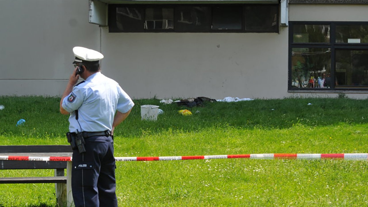 Ein telefonierender Polizist steht vor einer Absperrung vor einer Schule (Archivbild)