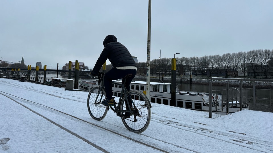 Ein Mann fährt auf Fahrrad bei Schnee an der Weser entlang 