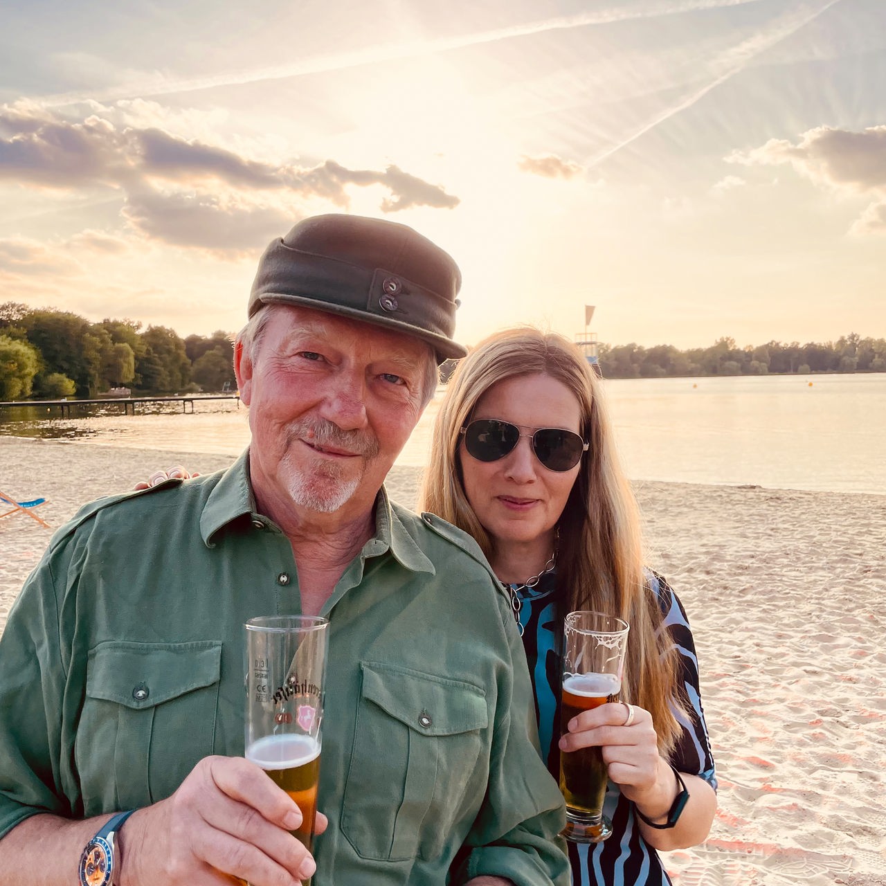 Dietmar Wischmeyer  und Tina Voß stehen mit einem Glas Bier in der Hand an einem See.